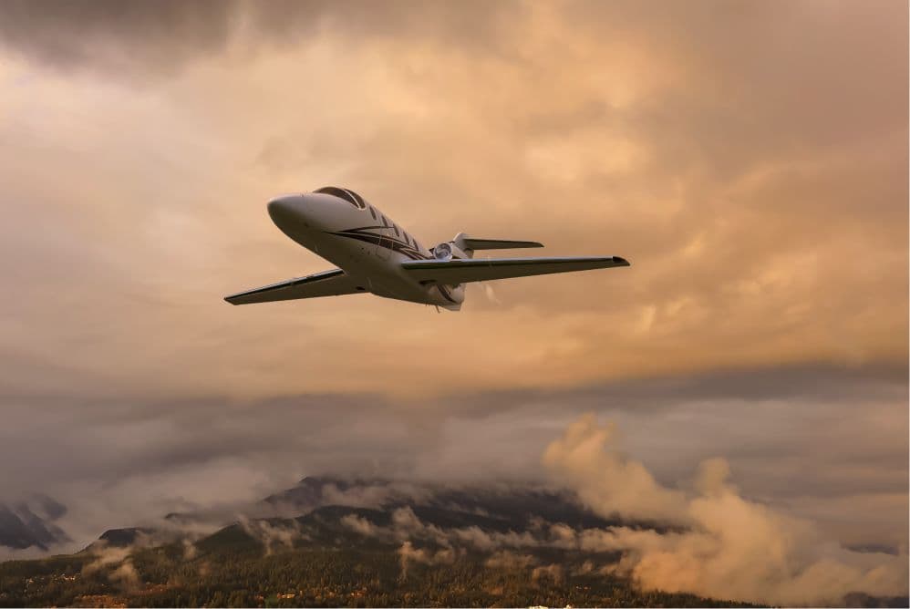 Private jet flying over mountains at sunset